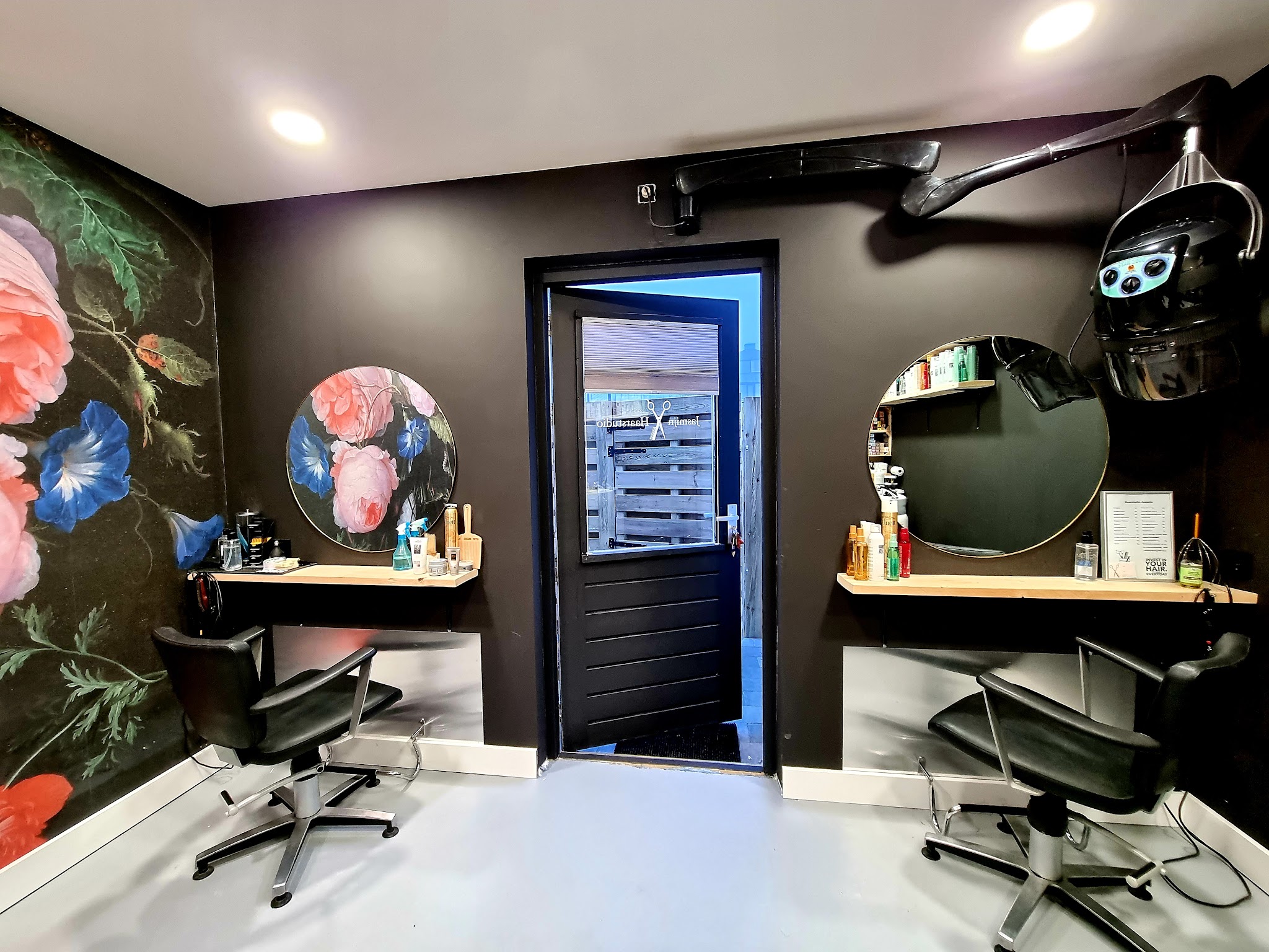 De salon met ronde spiegels, kappersstoelen en een bloemenwand